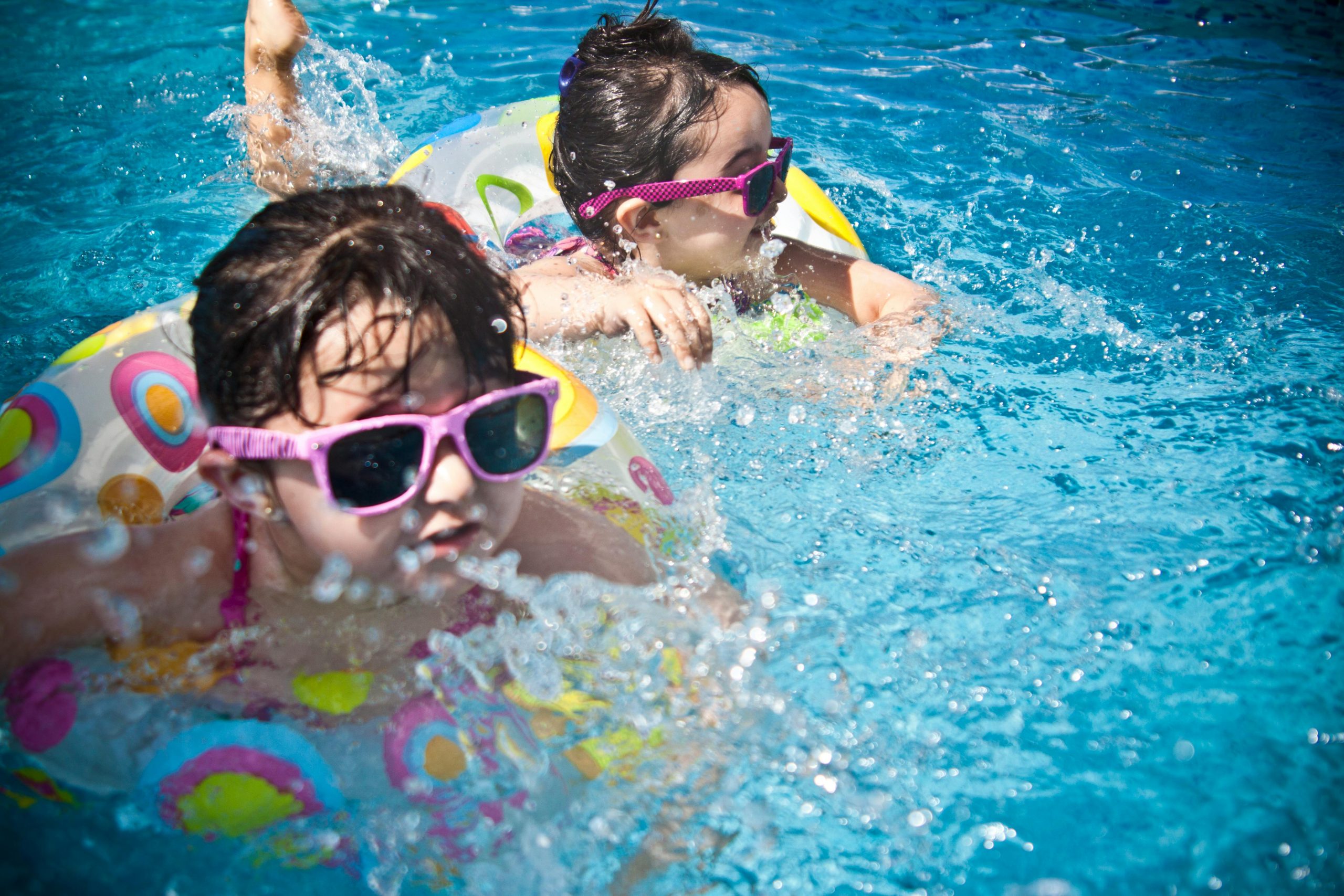 pexels-photo-61129-61129 Two young girls enjoying a playful day in a bright blue swimming pool with colorful float rings.